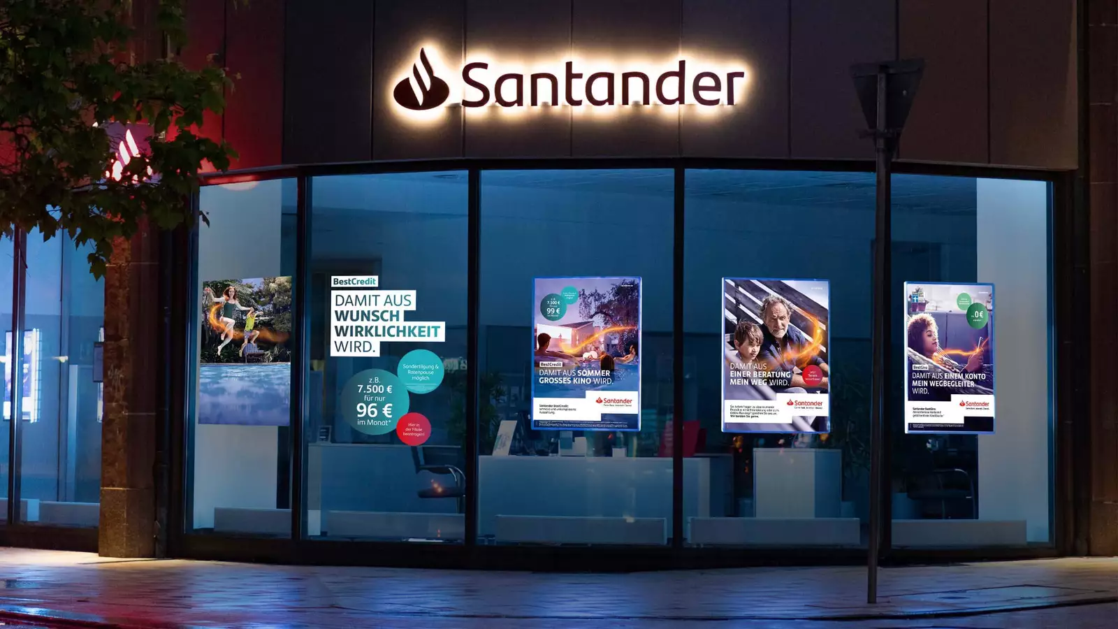 Das Bild zeigt beleuchtete Werbeplakate an den Fenstern der Santander Bank selbst.