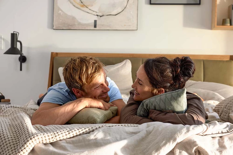 Ein Bild aus dem ADA Shooting auf welchem ein Paar auf dem Bauch auf einem Bett liegt und sich anlächelt. 
