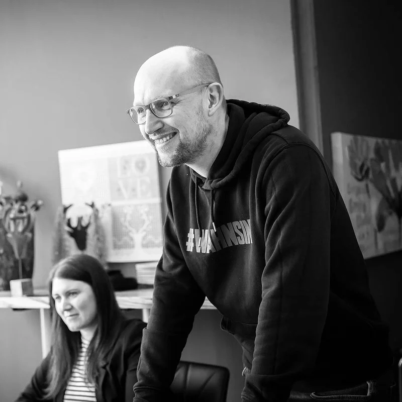 Zwei Mitarbeiter in einem Büro schauen lächelnd auf etwas außerhalb des Bildes.