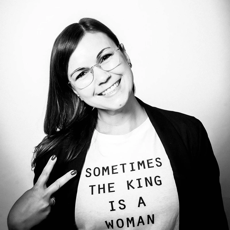 Eine Frau mit Brille posiert lächelnd vor der Kamera einer Fotobox und zeigt dabei mit ihrer rechten Hand ein peace Zeichen. Auf ihrem Shirt steht: Sometimes the king is an woman.